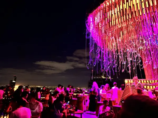 Rooftop bar nocą, różowe światła i tłum gości